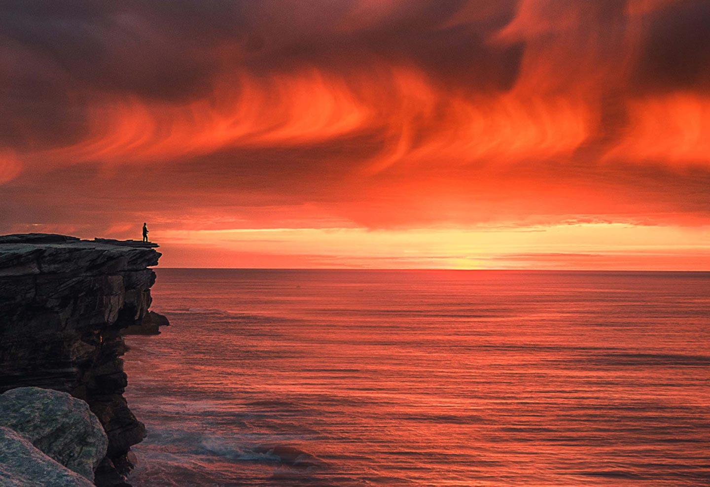 Person on a cliff overlooking the sea and sunset